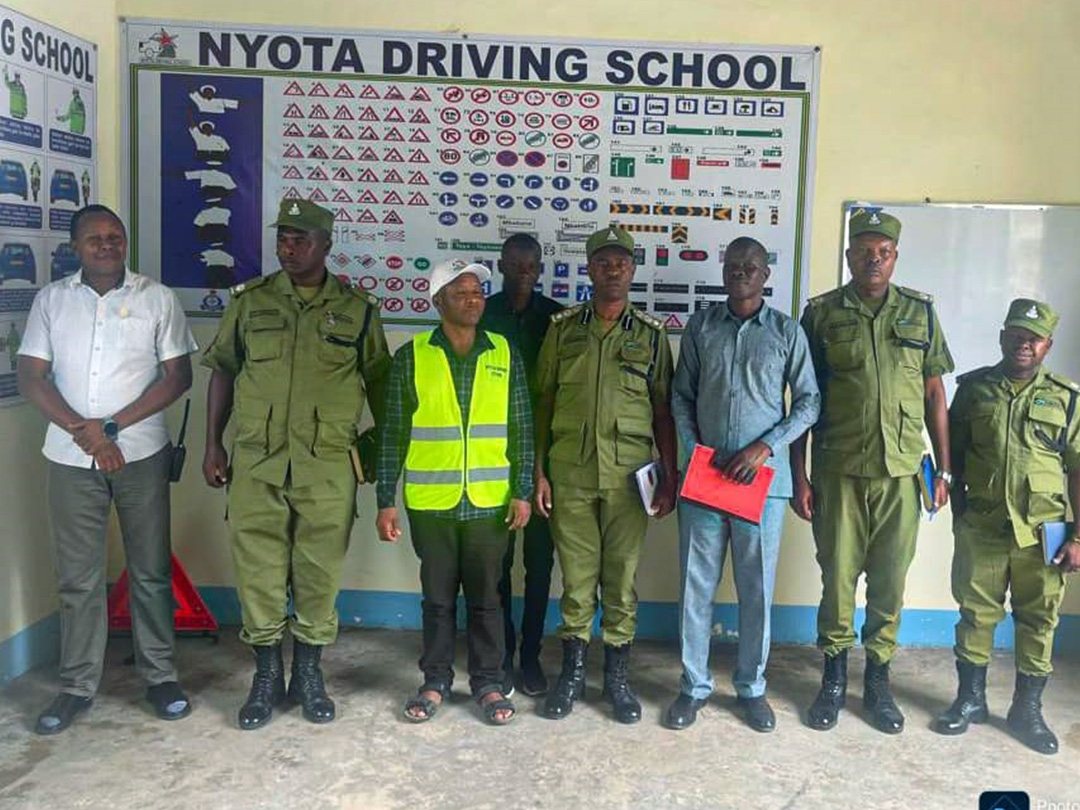 Traffic police officers standing with Nyota staff in front of the road-signs chart in our Mkuyuni classroom
